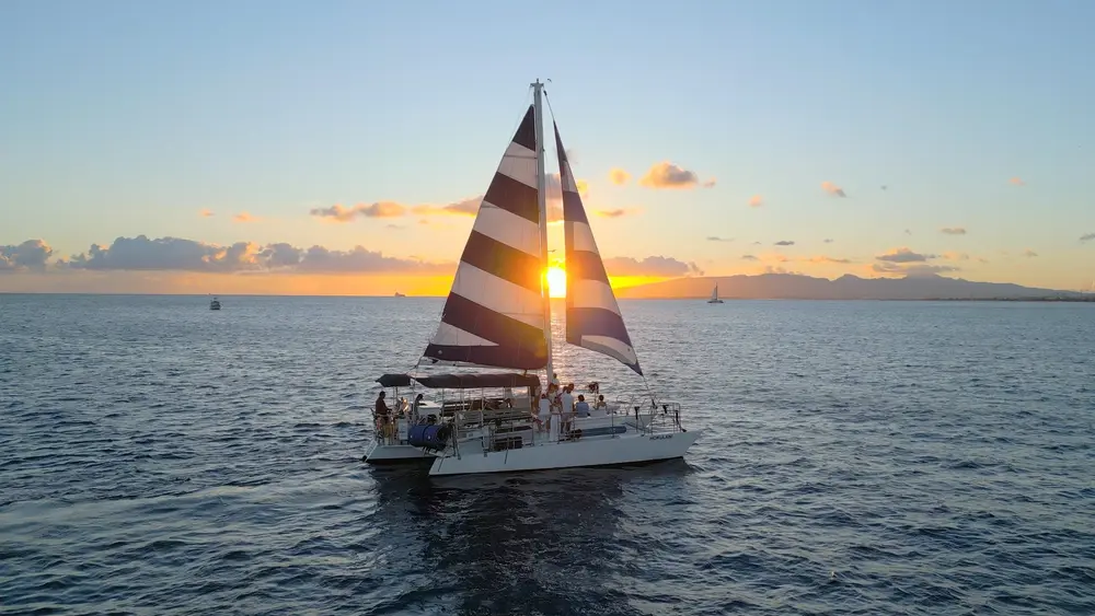 Three Tiki striped-sail catamaran at sunset off Waikiki