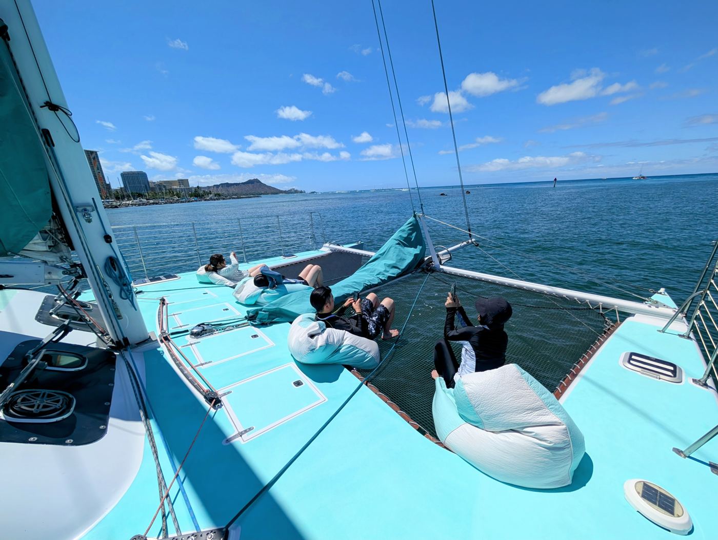 Guests stretched out on the catamaran net with Diamond Head in the distance